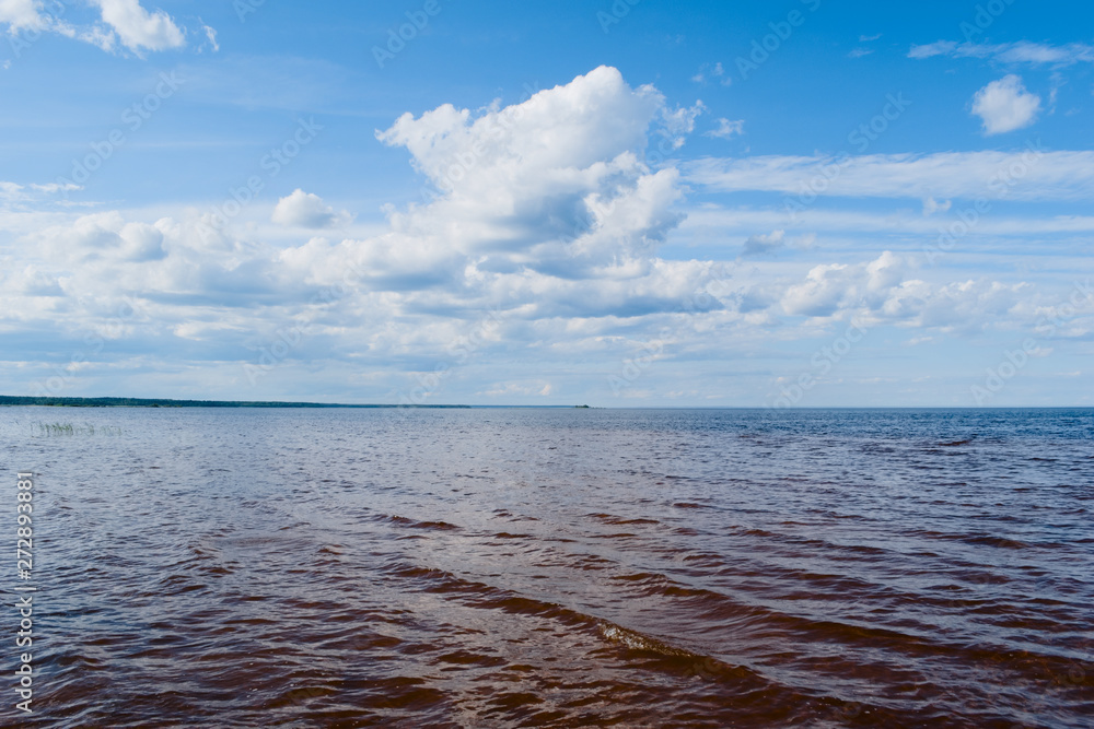 Obraz premium Lake Ladoga in the summer sunny day, reveals its open spaces for tourists. Clear water, combined with orange sand at the bottom of the lake, shows the bright boundaries of the depth of the lake.