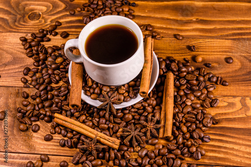 Cup of hot coffee, star anise, cinnamon sticks and scattered coffee beans on wooden table