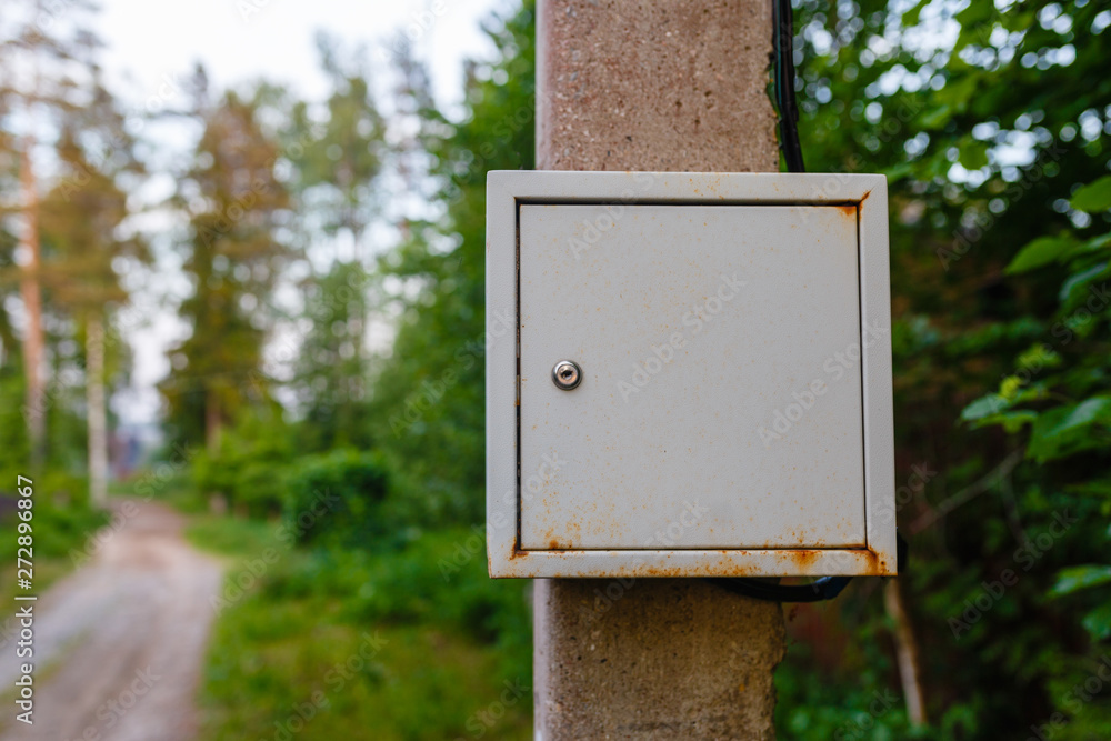 Old electric shield on a concrete pole in the countryside near a dirt road. The old electric shield, a rusty metal box hangs on the pole electric pole of the garden Old electric shield on a concrete pole in the countryside near a dirt road. The old electric shield, a rusty metal box hangs on the pole electric pole of the garden