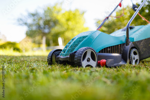 Electric lawn mower cuts moss and green grass. The alignment of the green lawn with the mower. Close-up in front of a green lawn mower on wheels on the background of the garden