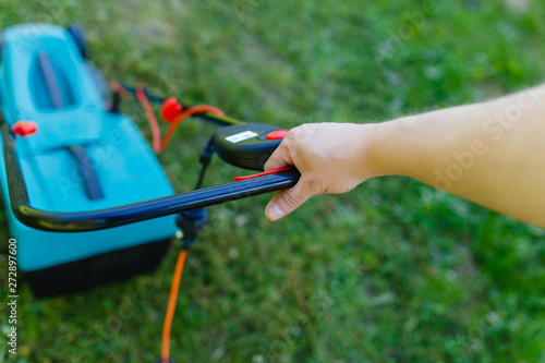 Man hand holding electric lawn mover machine to cutting short green grass.(Focus on the hands and handle of the lawn mower)
