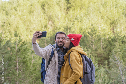 Young happy funny couple man and woman makes selfie on smartphone; forest on the background; travel concept.