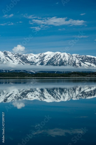 Snow covered mountains reflecting in calm lake with beautiful blue sky and clouds