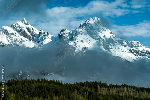 Snow covered rocky mountain peaks with dramatic clouds and blue sky © Elizabeth