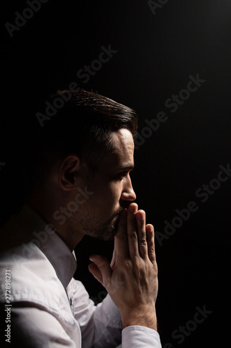 Handsome bearded man praying. Low light portrait. Black background.