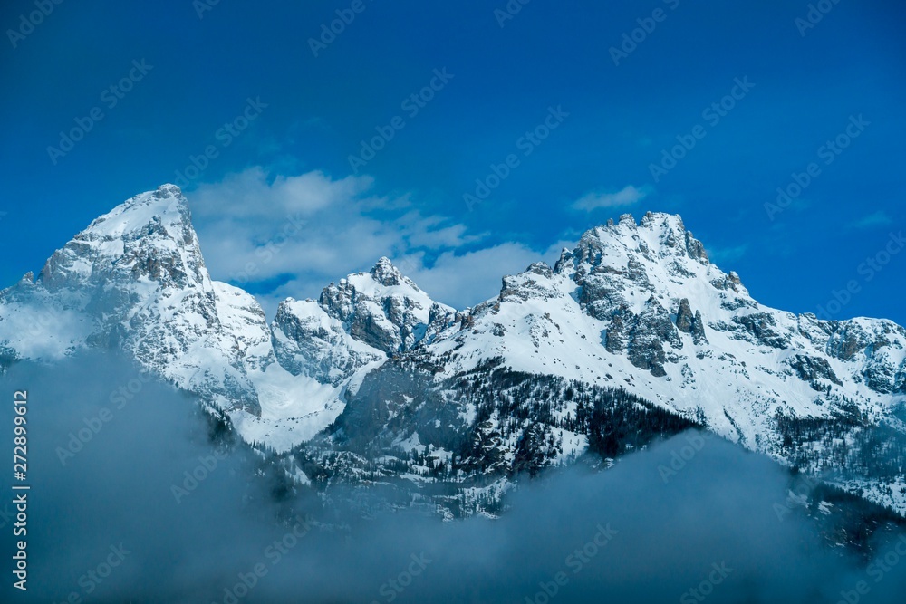 Obraz premium Snow-covered rocky mountain peaks surrounded by misty clouds 