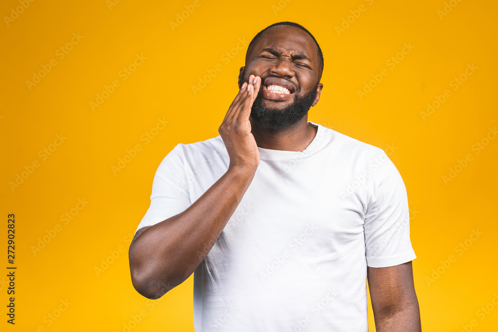 Indoor photo of young African American african man isolated on yellow background suffering from terrible pain in teeth, showing it on his face vividly, looking troubled and distressed. Indoor photo of young African American african man isolated on yellow background suffering from terrible pain in teeth, showing it on his face vividly, looking troubled and distressed.