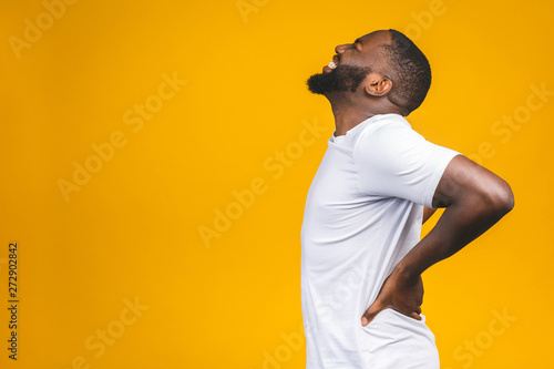 Young afro american young man suffering from backache for having made an effort on isolated background.