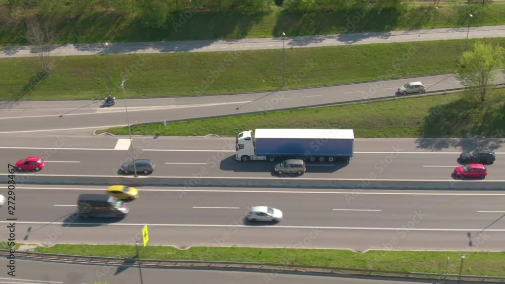 AERIAL: Congested summer traffic moving along the expressway and under the railroad tracks. Flying along a white cargo truck and cars driving down the asphalt highway and under the railway overpass. AERIAL: Congested summer traffic moving along the expressway and under the railroad tracks. Flying along a white cargo truck and cars driving down the asphalt highway and under the railway overpass.