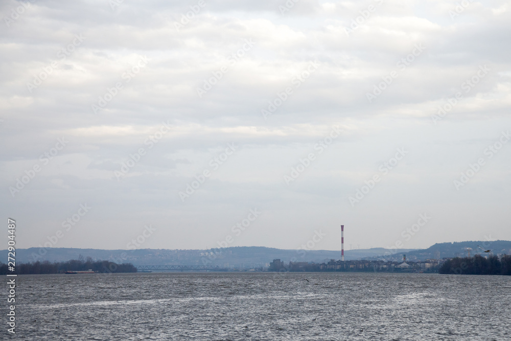 Belgrade under the rain seen from Zemun, with an industrial chimney in background in front, on the Danube river, and seagulls flying in front