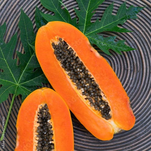Fresh orange papaya with papaya green leaves on a  brown background. Tropical Fruit. Top view. Free text space.