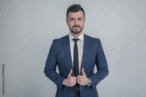 Portrait of a charming mature businessman dressed in suit posing while standing and looking at camera isolated over gray background