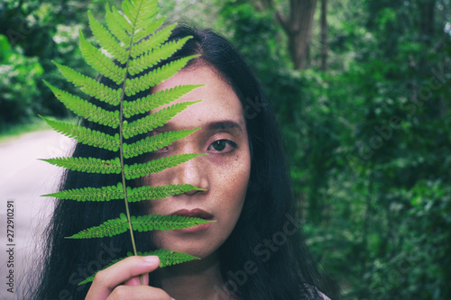 Beautiful young woman closeup face with natural make up and frackles posing front of plant tropical green leaves background with fern photo