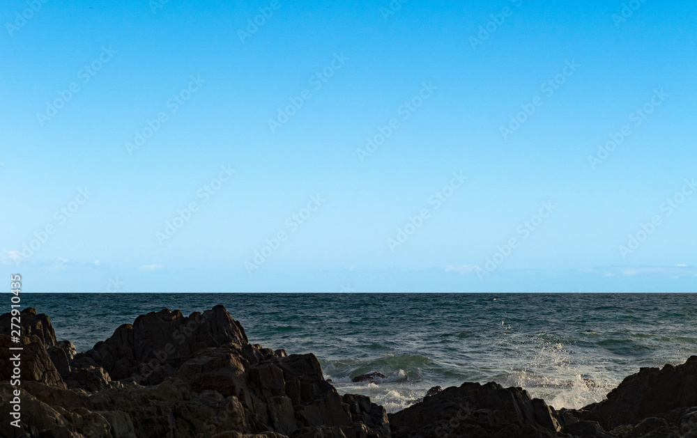 Seascape. Blue clear sky and black rock. Calm sea