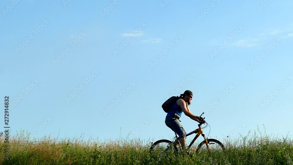 Teenager with a backpack on a bicycle. Walking outside the city. Tall grass slow motion Teenager with a backpack on a bicycle. Walking outside the city. Tall grass slow motion