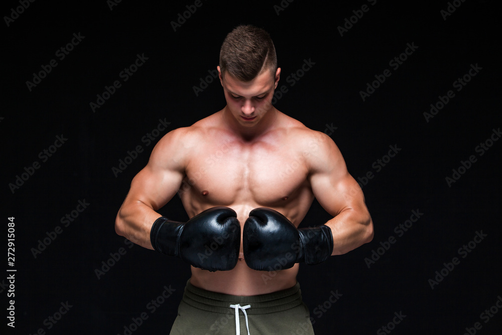 Muscular young man in black boxing gloves and shorts shows the different movements and strikes in the studio on a dark background. Strong Athletic Man - Fitness Model showing his perfect body. Copy