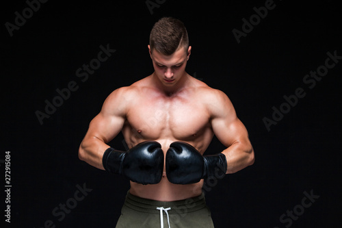 Muscular young man in black boxing gloves and shorts shows the different movements and strikes in the studio on a dark background. Strong Athletic Man - Fitness Model showing his perfect body. Copy