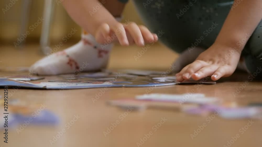 A small child, collecting puzzles sitting on the floor in the room. Close-up of the child's hands. A small child, collecting puzzles sitting on the floor in the room. Close-up of the child's hands.