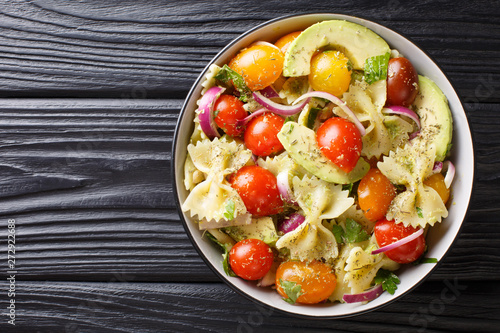 Pasta Farfalle with ripe avocado, onions and tomatoes close-up in a bowl. horizontal top view