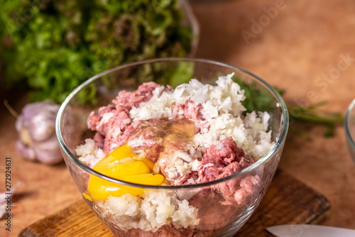 Minced meat with chopped onion and raw egg in a glass plate.