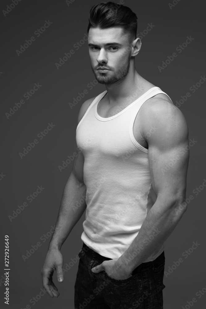Naklejka premium young man with a beard. A man in a t-shirt. Male portrait on a gray background. Stylish man. black and white photo. Sports man. male fitness model. studio portrait
