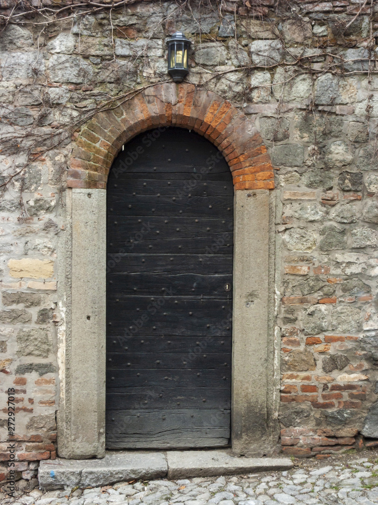 Antique door with wooden plank panels of a rural house, with iron fixing parts, Italy.