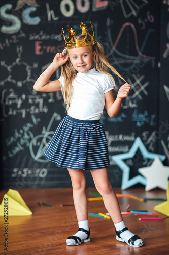 cute little schoolgirl against chalkboard with school formulas, with a gold crown on her head