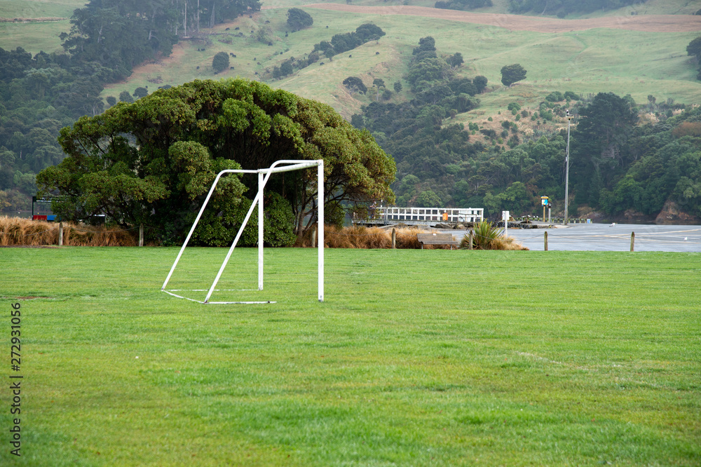 White soccer goal and green grass field with big tree and mountain background. White soccer goal and green grass field with big tree and mountain background.