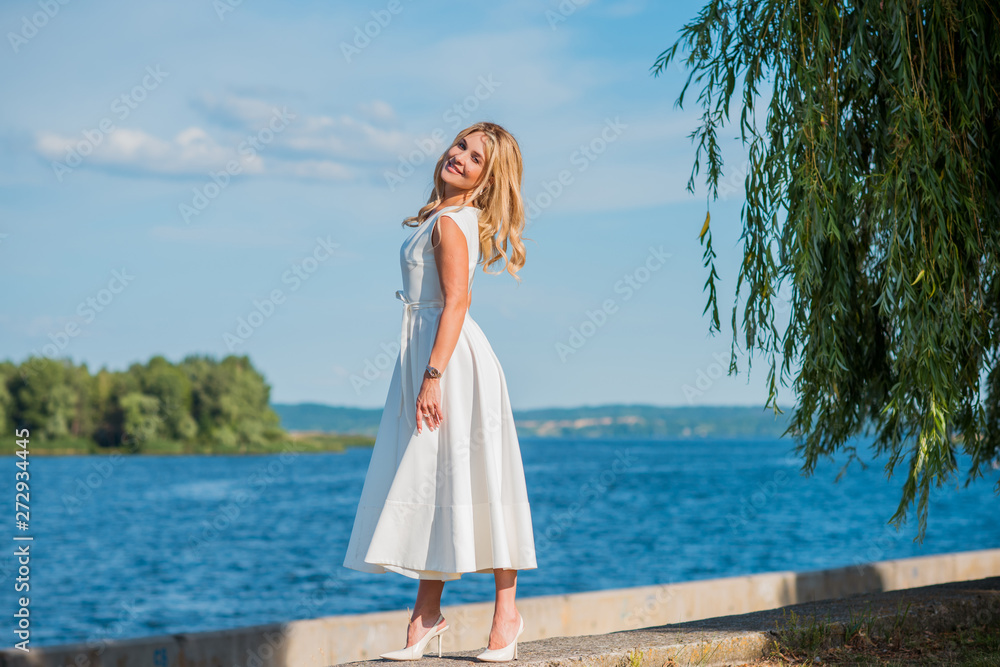 Elegant blonde hair woman in white midi dress at shore. Concept oа white code, fashionable lady, pretty dress and clothes 