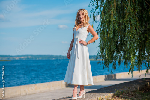 Elegant blonde hair woman in white midi dress at shore. Concept oа white code, fashionable lady, pretty dress and clothes 