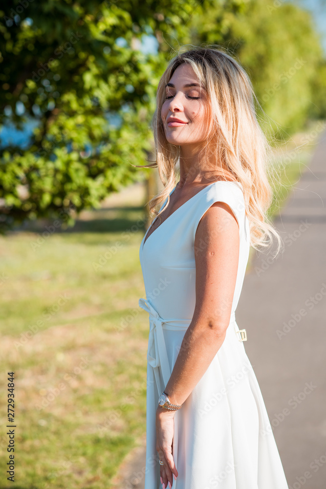 Elegant blonde hair woman in white midi dress at shore. Concept oа white code, fashionable lady, pretty dress and clothes 