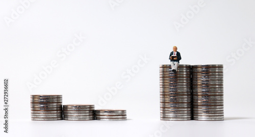 Miniature people sitting on piles of coins. photo