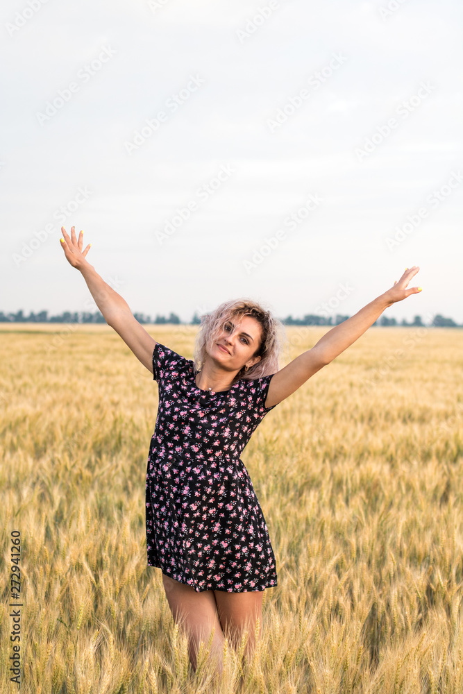 young tanned curly haired woman in dress is happy to be on the field of ripened wheat, sunset time young tanned curly haired woman in dress is happy to be on the field of ripened wheat, sunset time