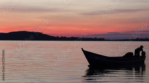 Silhouettes of two young fishermen on a small wooden boat on Lake Victoria under orange sky after sunset. Boat slowly floats out of frame. photo