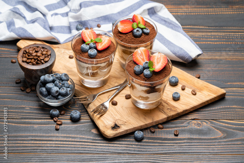 Classic tiramisu dessert with blueberries and strawberries in a glass on wooden background photo