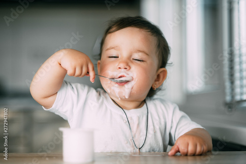 A little charming girl eats yogurt all smeared herself
