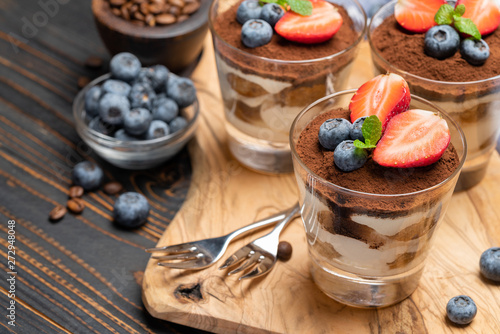 Classic tiramisu dessert with blueberries and strawberries in a glass on wooden background