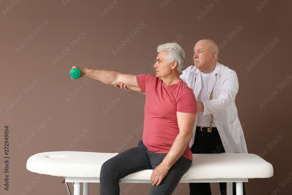 Obraz premium Senior physiotherapist working with mature man on color background