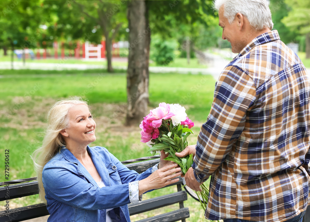 Mature woman receiving flowers from her husband in park