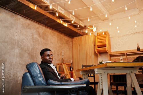 Strong powerful african american man in black suit sit in couch at cafe.