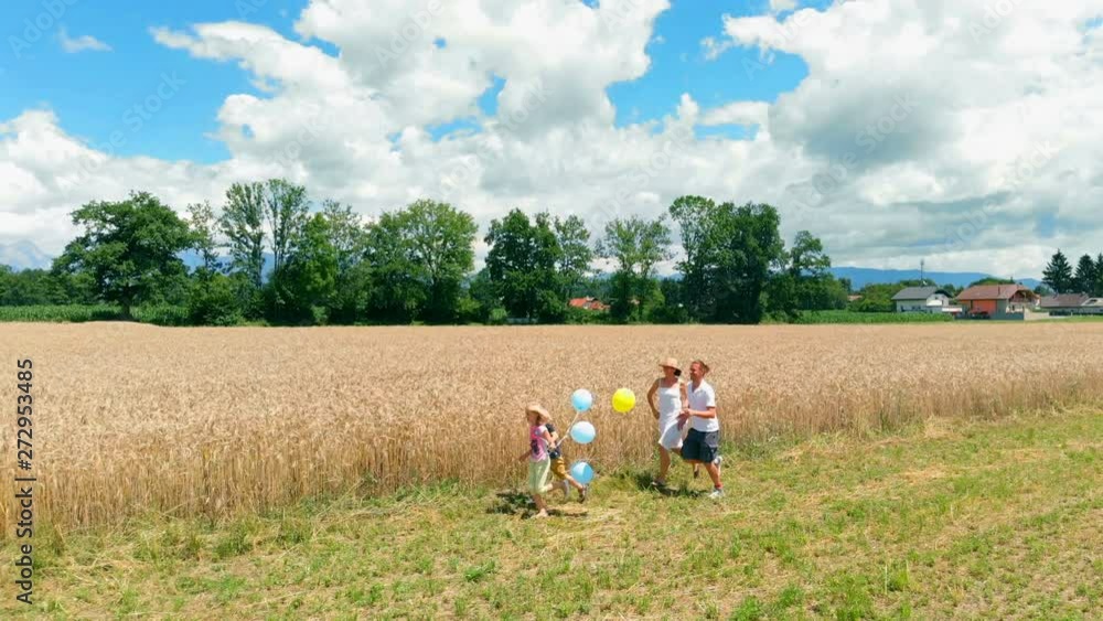 A young family is walking across the fields and then they start running. A girl is carrying balloons of different colours. A young family is walking across the fields and then they start running. A girl is carrying balloons of different colours.