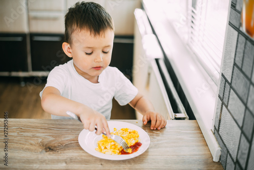 a child in a t-shirt in the kitchen eating an omelet with a fork is very tasty