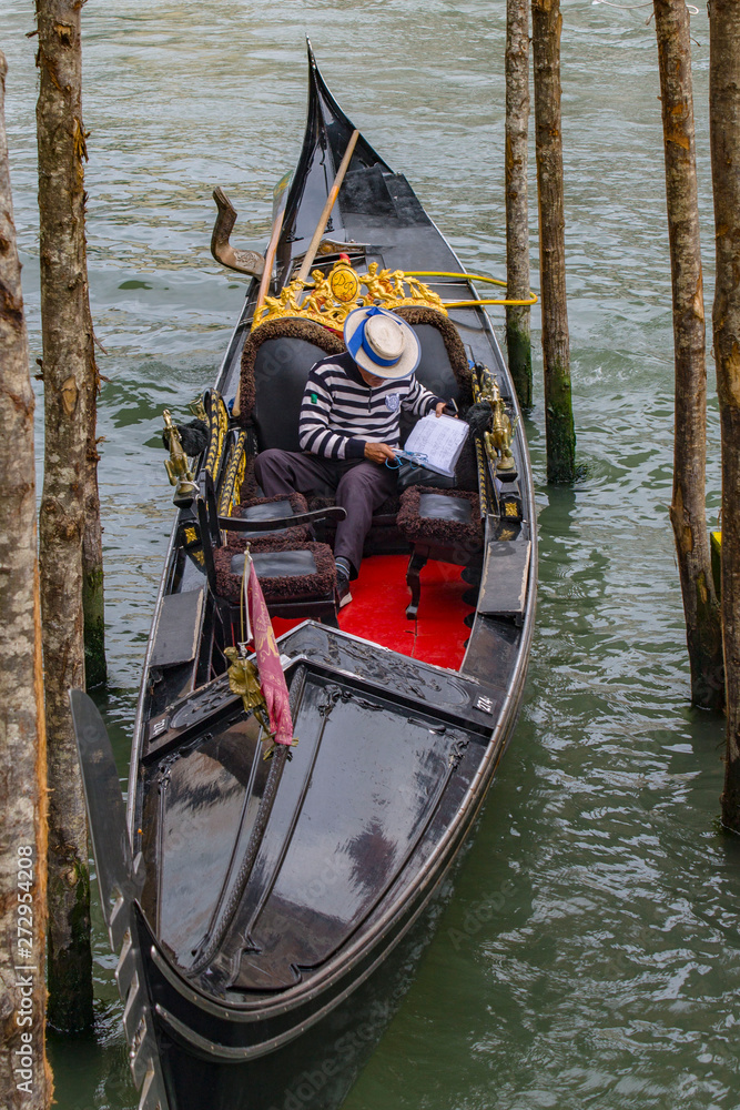 Gondolier and gondola at the pier. A bright sunny day in Venice, Italy. Historical transprot and the traditional male profession of Venice.