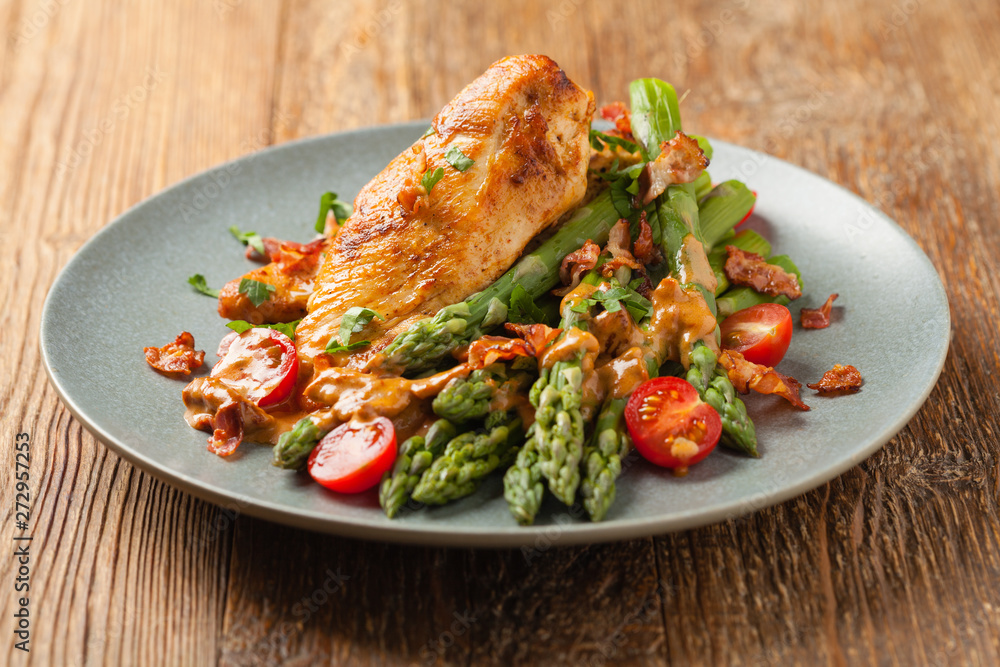 Roasted chicken breast, served on asparagus with tomato sauce, dried tomatoes. Front view. Roasted chicken breast, served on asparagus with tomato sauce, dried tomatoes. Front view.