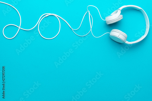 White headphones with cable. Top view of headphones on turquoise blue background. Minimalist photo of earphones with copy space. White dj headphones with cable in upper part of blue background
