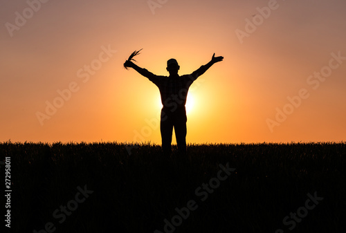 Silhouette of senior farmer standing in field with his hands outstretched.