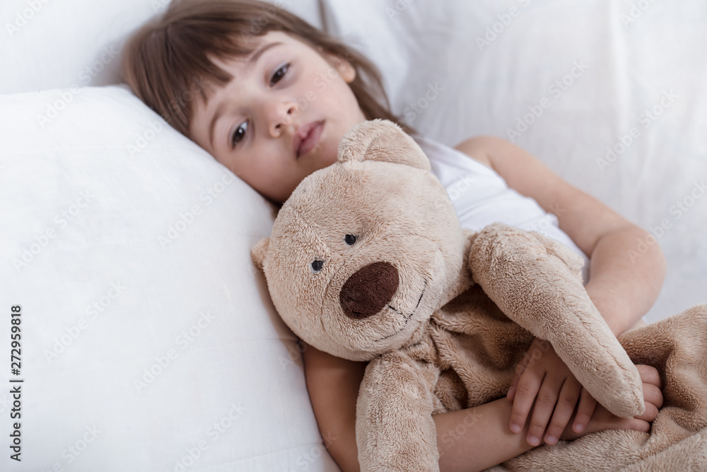 Cute little girl smiling while lying in a cozy white bed Cute little girl smiling while lying in a cozy white bed