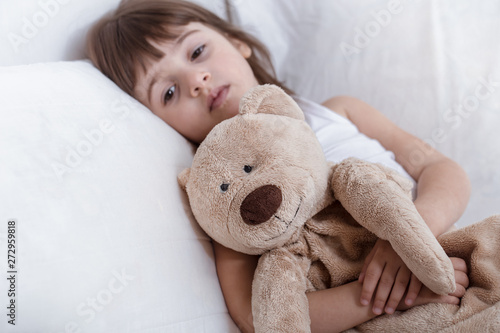 Cute little girl smiling while lying in a cozy white bed