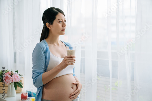 asian young pregnant woman in white sport bra holding glass of fresh milk and touching her belly with hands. beautiful elegant lady motherhood standing by window watching urban view outdoors at home Free Download asian young pregnant woman in white sport bra holding glass of fresh milk and touching her belly with hands. beautiful elegant lady motherhood standing by window watching urban view outdoors at home - GFXLoad