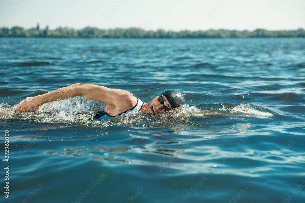 Professional triathlete swimming in river's open water. Man wearing swim equipment practicing triathlon on the beach in summer's day. Concept of healthy lifestyle, sport, action, motion and movement.